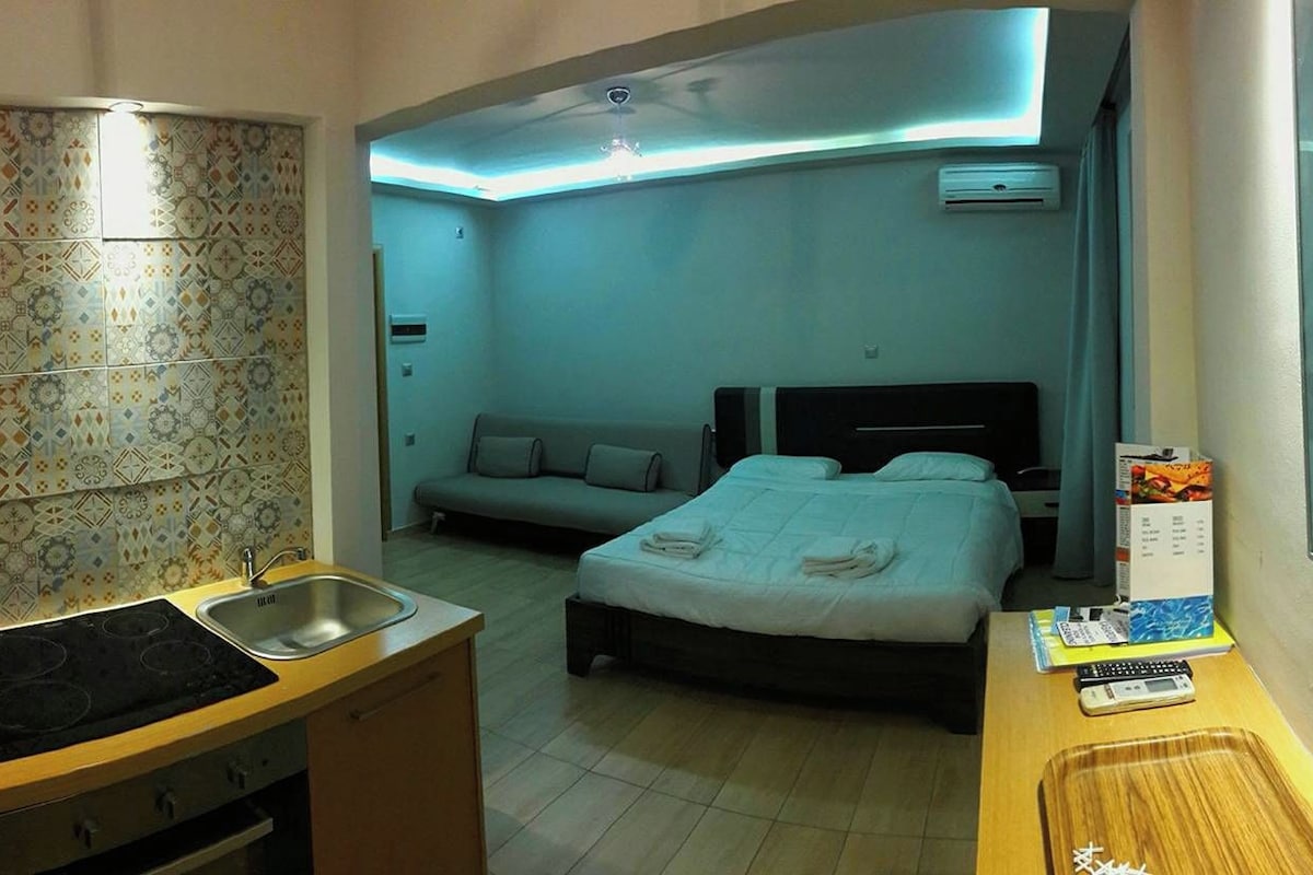 Habitació d'hotel petita amb cuineta, un llit, un sofà i una paret amb frases motivadores.