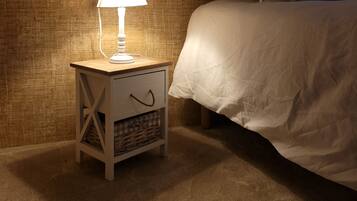 A neatly made bed with white bedding, a bedside lamp on a small wooden nightstand, and a textured wall behind.