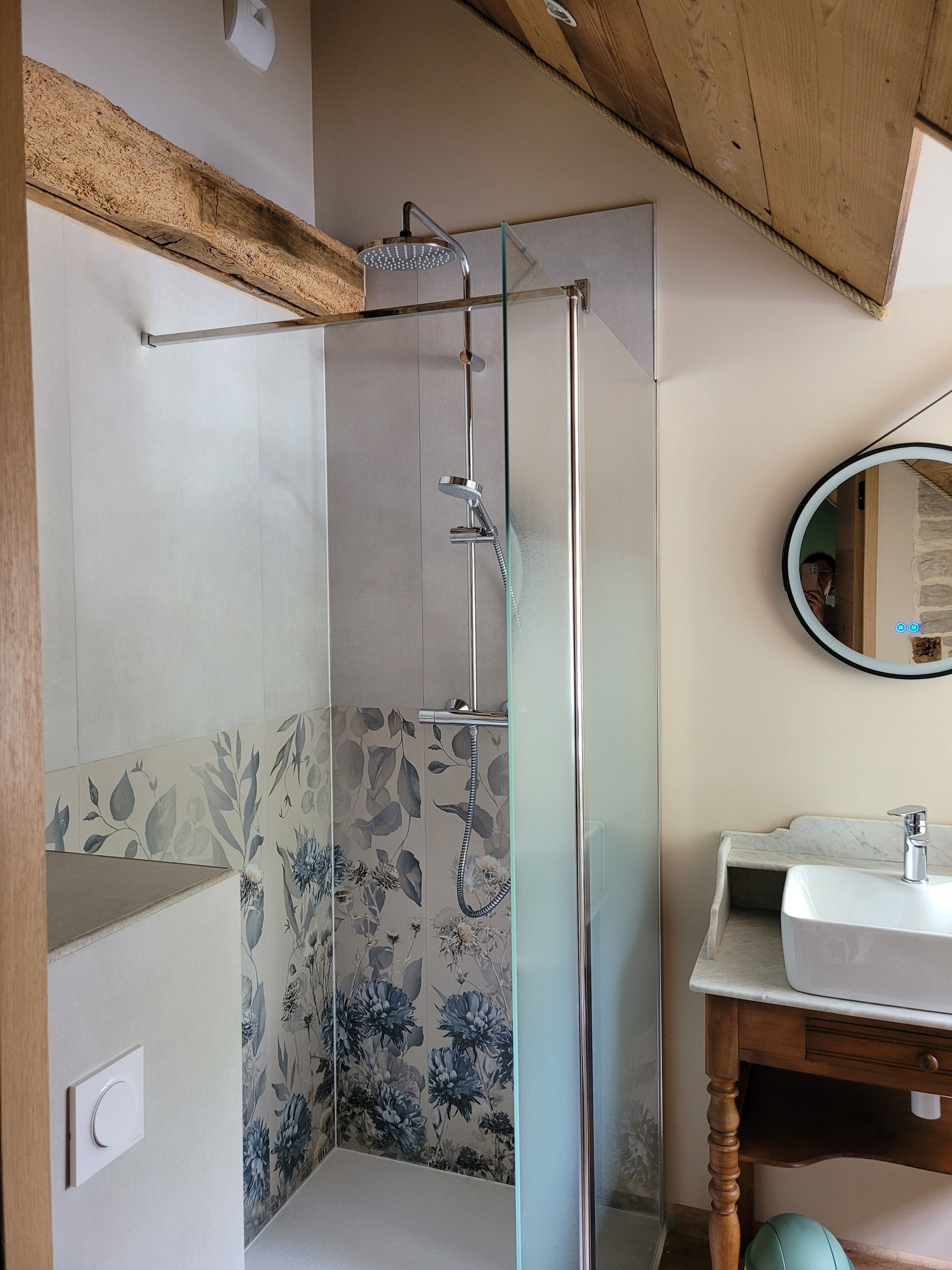 A modern bathroom with a glass-enclosed shower, a wooden ceiling, and a marble sink.