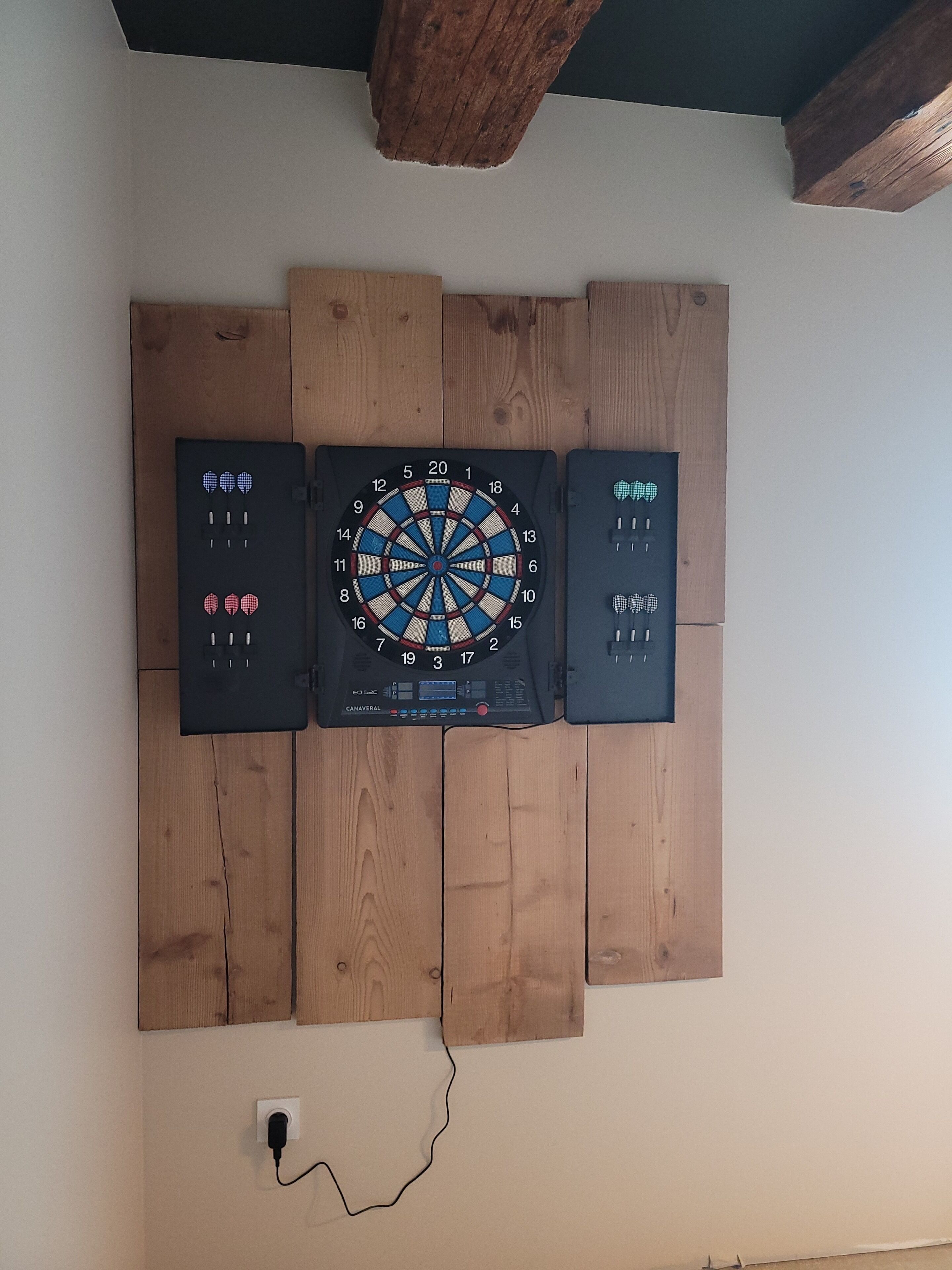 A dartboard mounted on a wooden wall with a power outlet below.