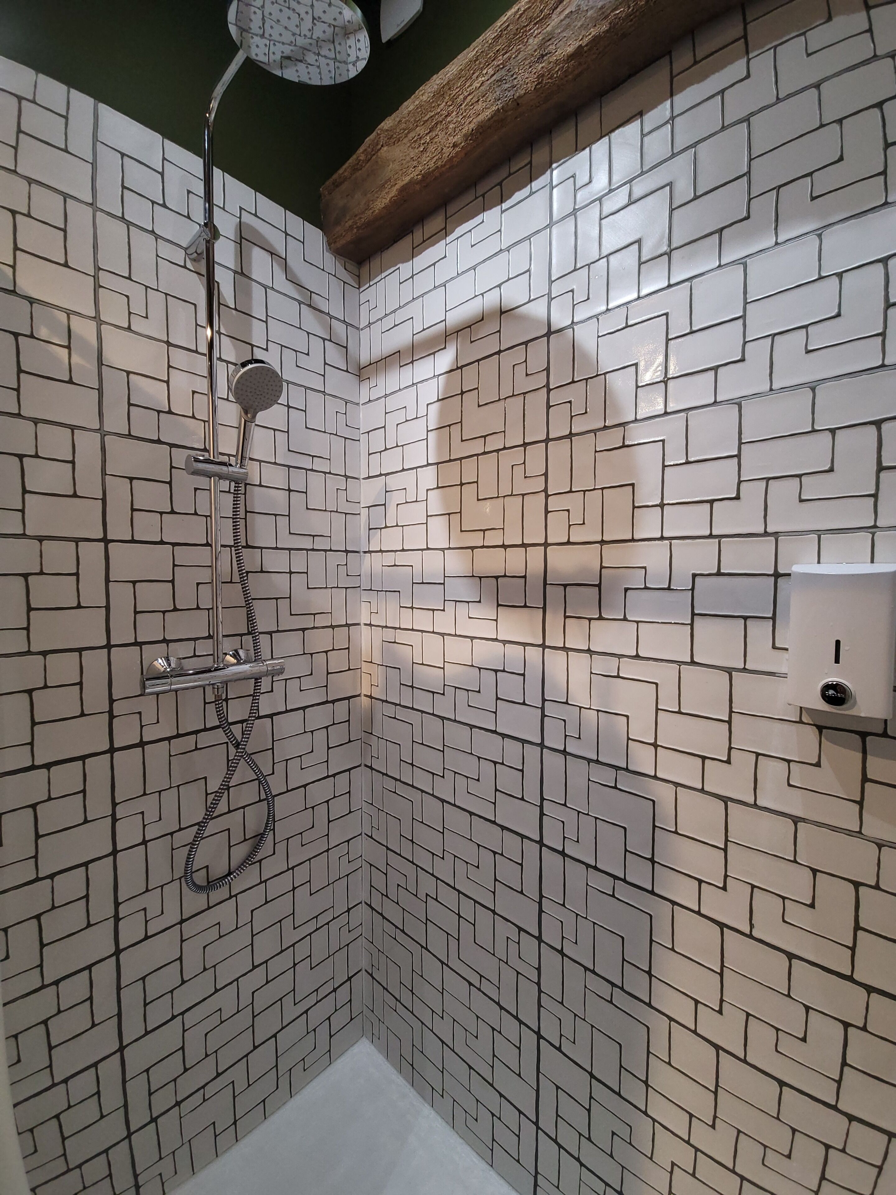 Une douche au design moderne, avec un motif géométrique sur les carreaux des murs et une étagère en bois au-dessus de la douche.
