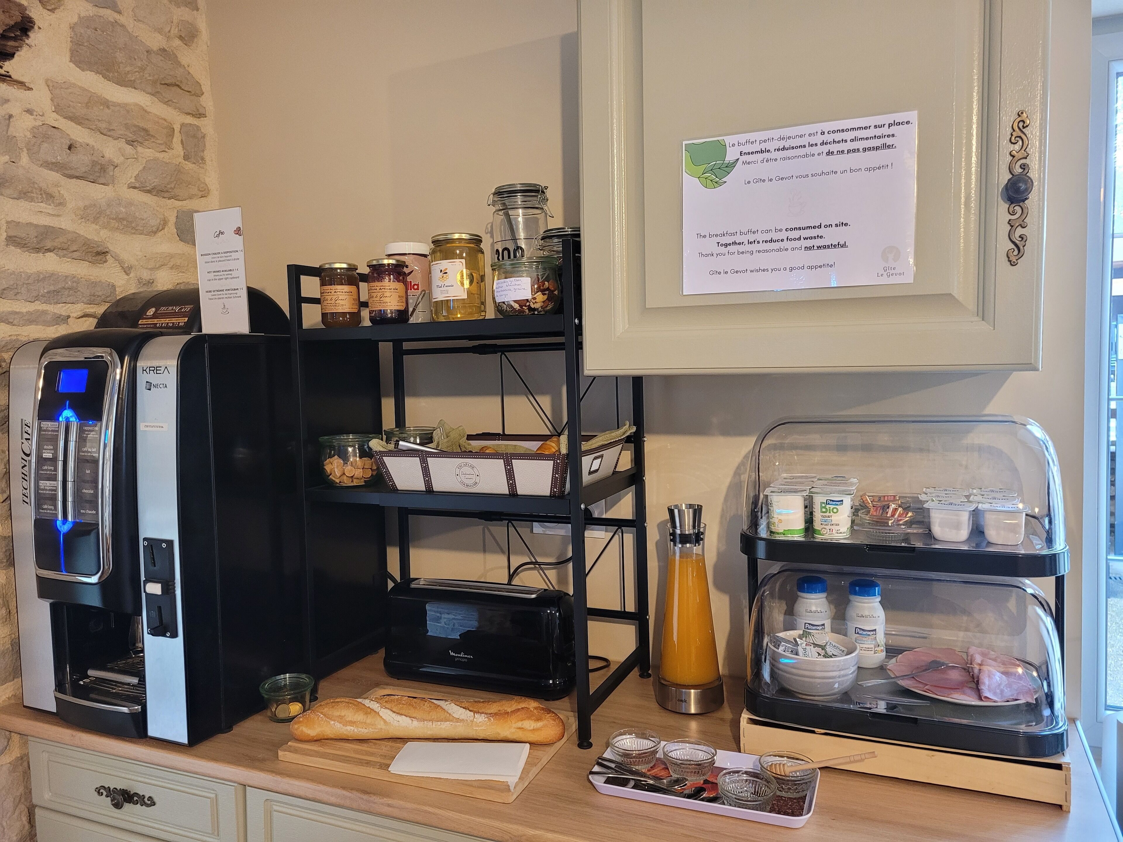 Montaje de un bufé de desayuno con una máquina de café, frascos de conservas y una variedad de alimentos a la vista.