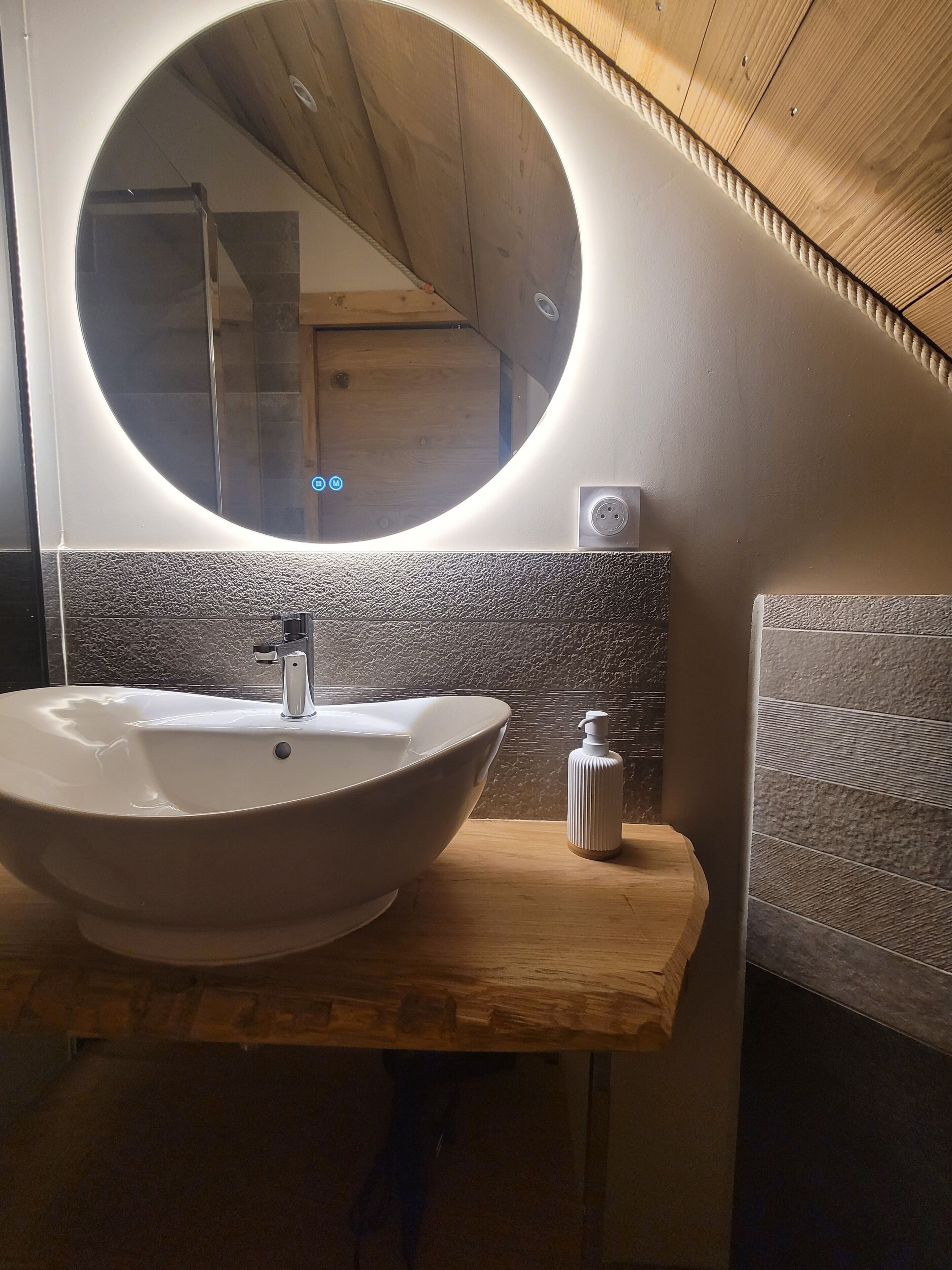 A modern bathroom with a large oval sink, a round mirror, and a wooden vanity.