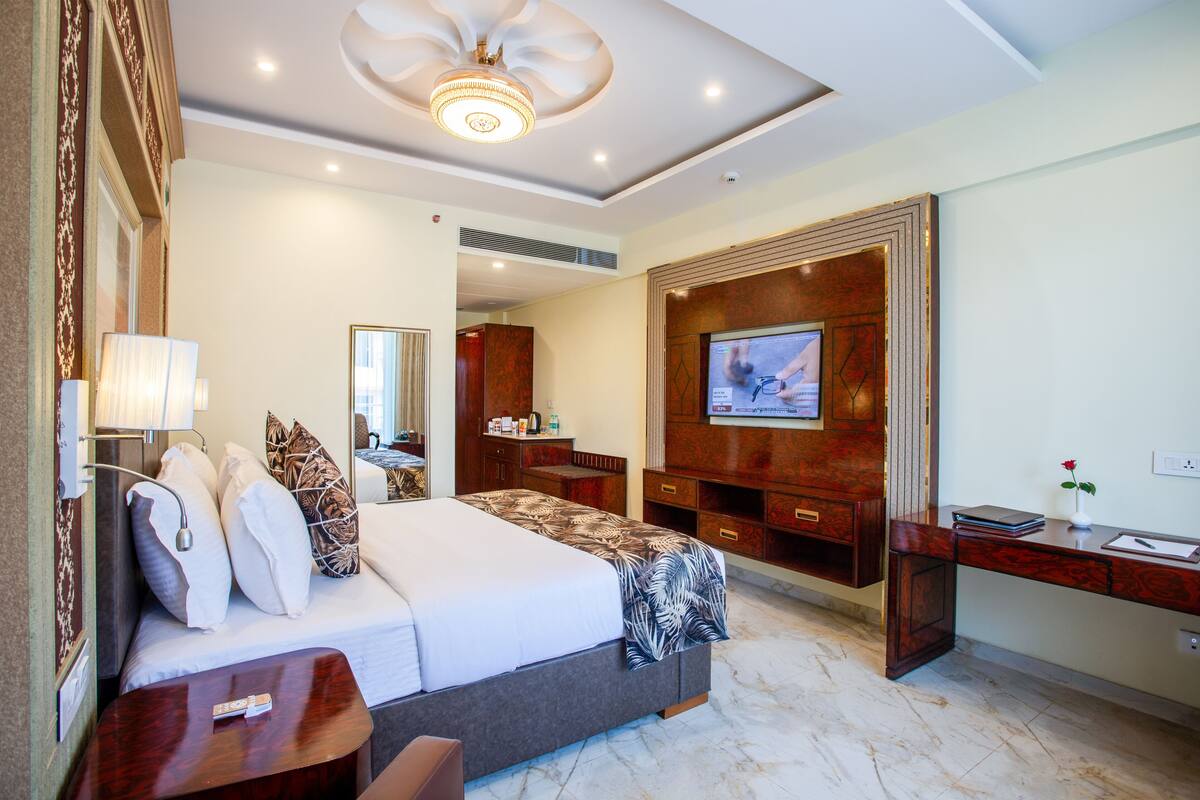 A hotel room with a large bed, a TV mounted on the wall, a desk, and a mirror.