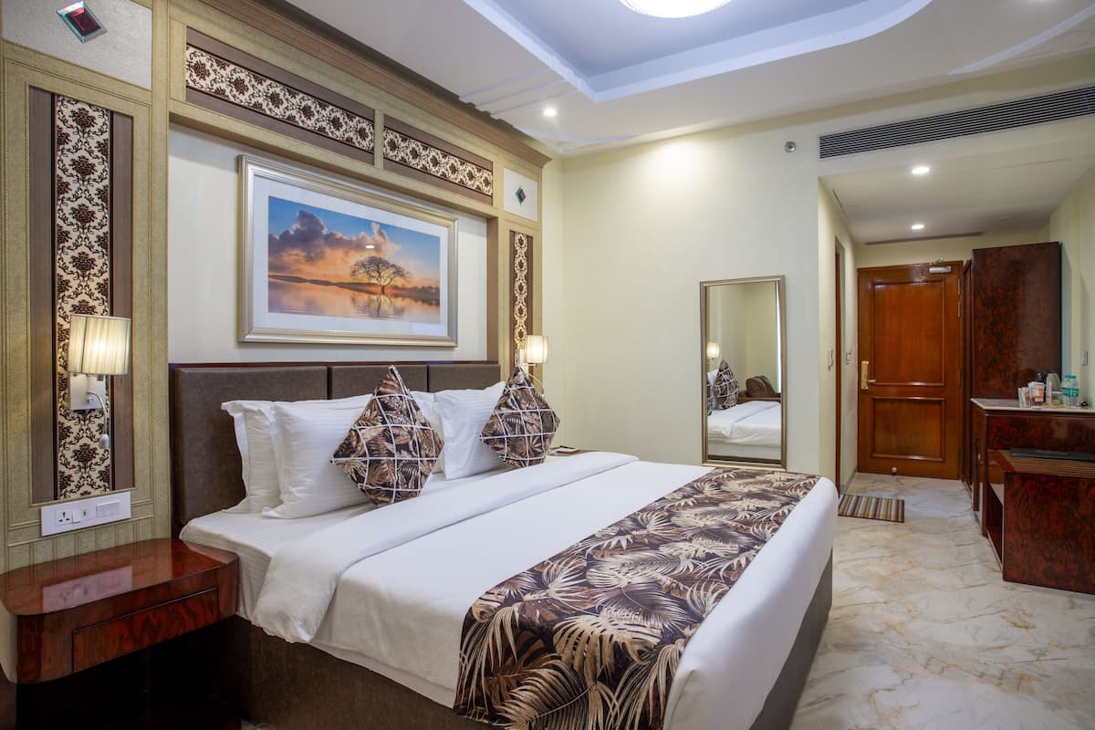 A hotel room with a large bed, a wooden dresser, a mirror, and a painting on the wall.
