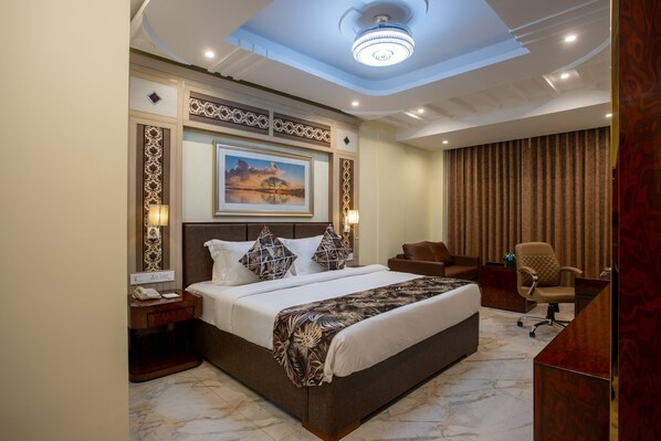 A hotel room with a large bed, a desk, and a chair. There is a painting on the wall and a chandelier on the ceiling. - The Avenue Grand (Calangute)