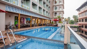 A hotel with a swimming pool, outdoor seating, and multiple balconies. - The Avenue Grand (Calangute)