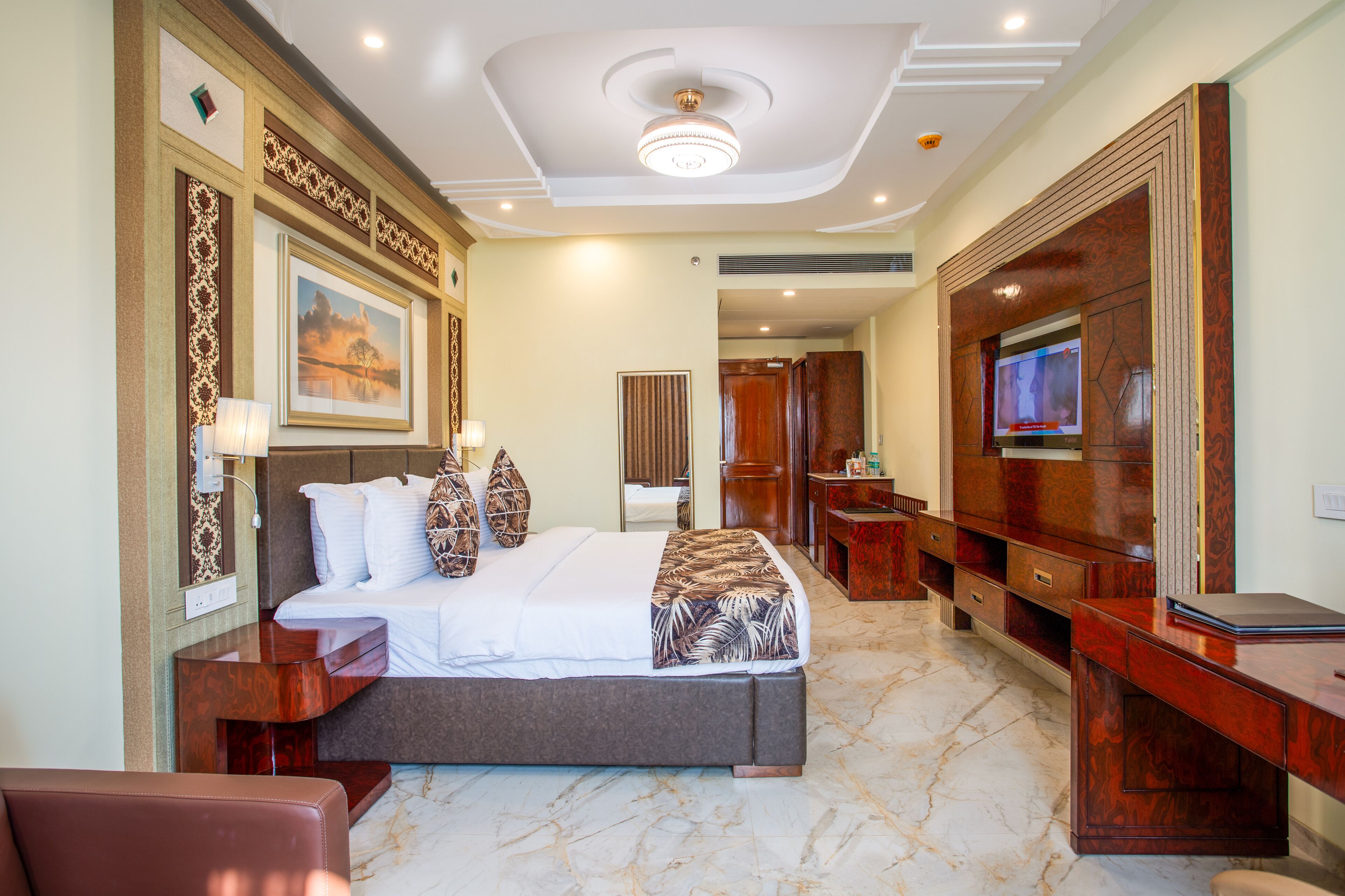A hotel room with a large bed, a TV, a desk, and a mirror.