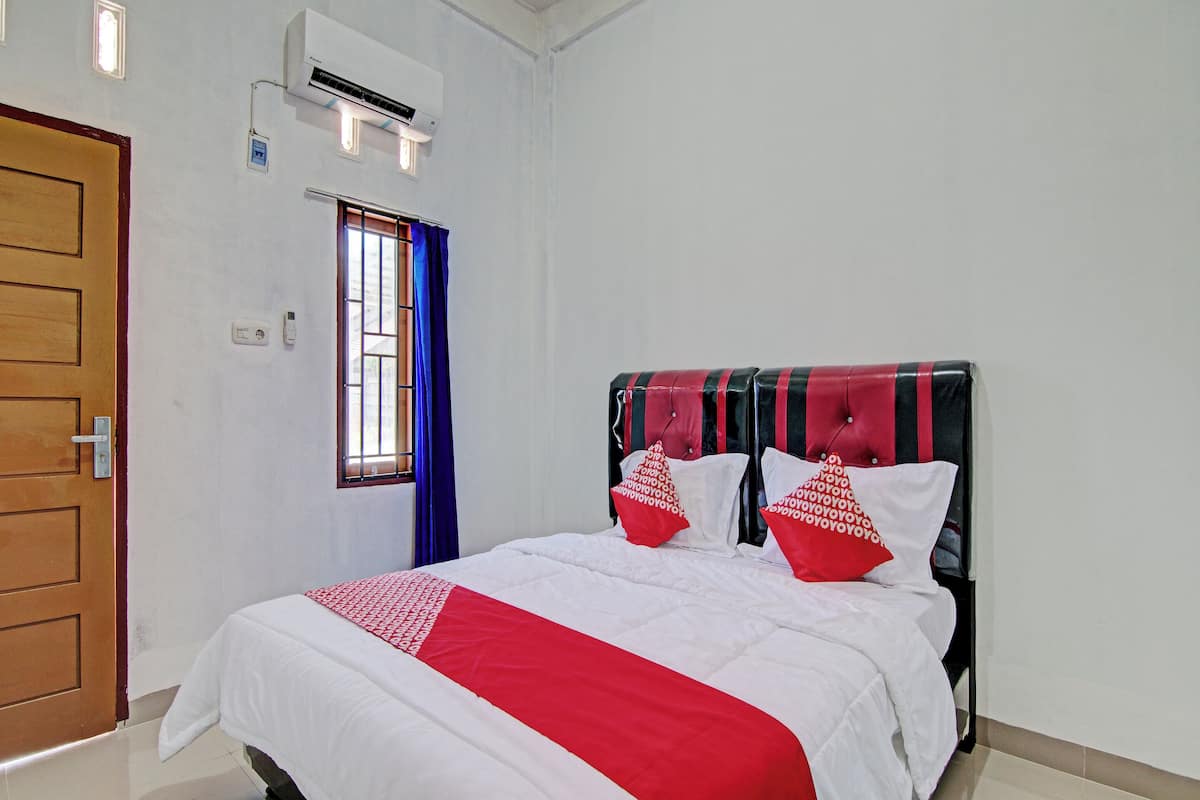 A hotel room with a bed, a window with blue curtains, an air conditioning unit, and a wooden door.
