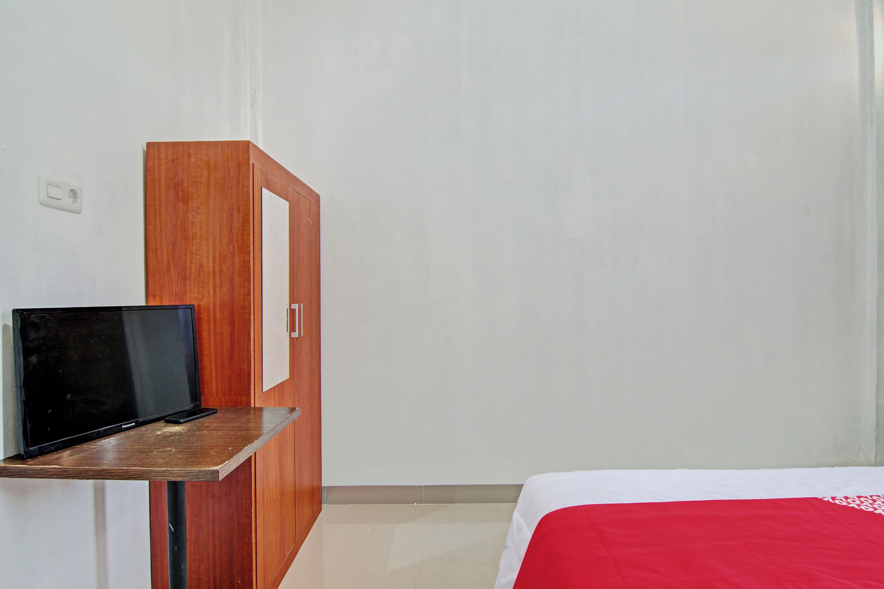 A hotel room with a bed, a wooden desk with a television, and a wardrobe.