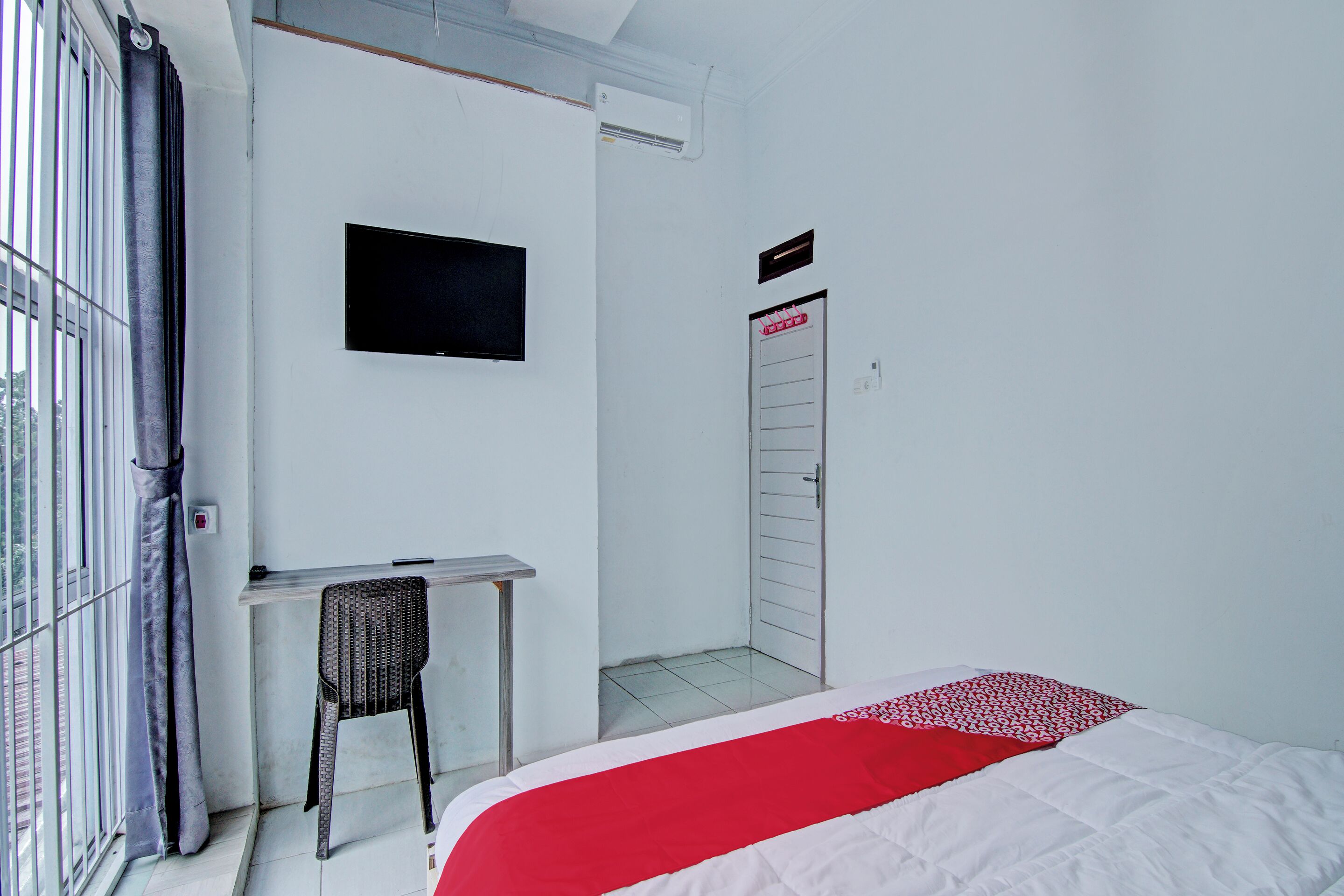 A room with a bed, a desk, a chair, a TV, and a door.