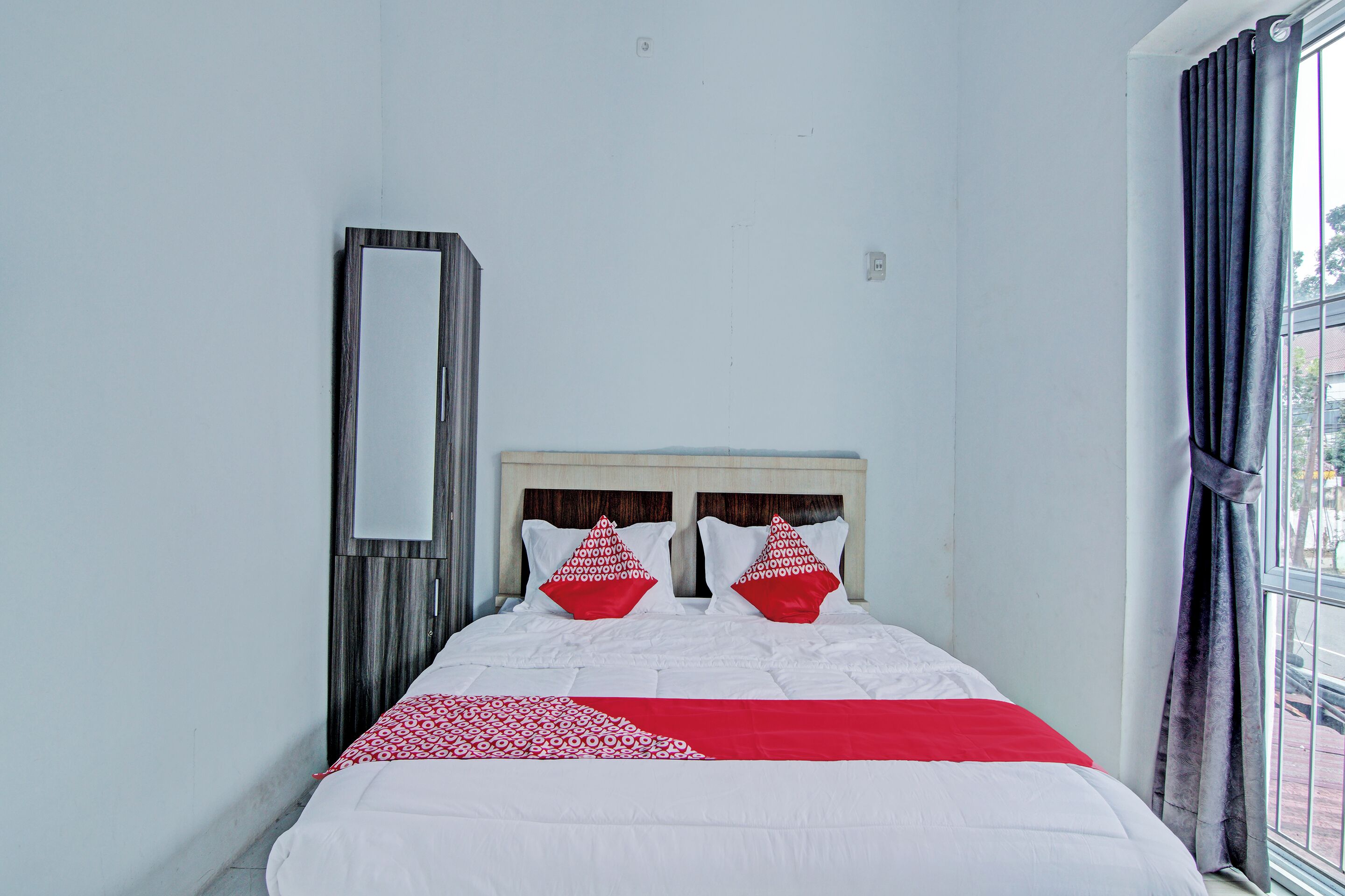 A neatly made bed with a white and red bedspread, two matching pillows, and a wooden headboard.