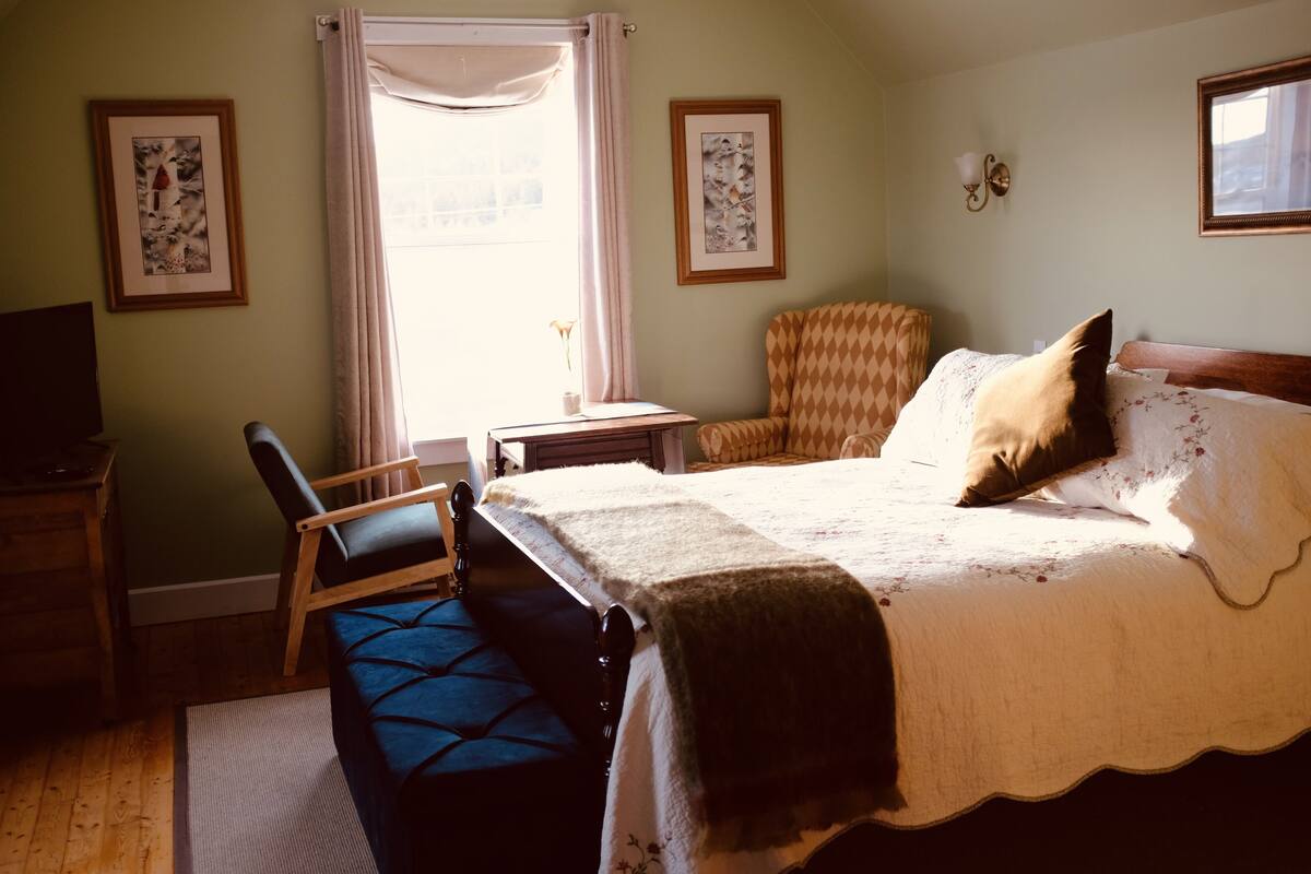 A bedroom with a bed, a chair, a desk, and a window.