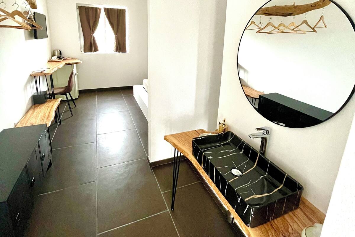 A modern, well-lit room with a wooden desk, a round mirror, and a black tray on a wooden table.
