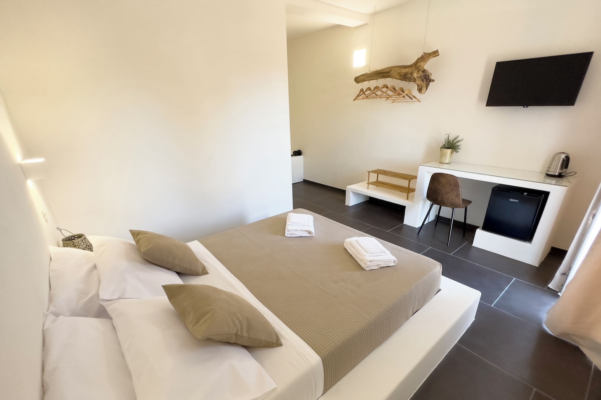 Una habitación de hotel moderna con una cama grande, un escritorio con silla, un televisor de pantalla plana y un pequeño rincón de descanso.