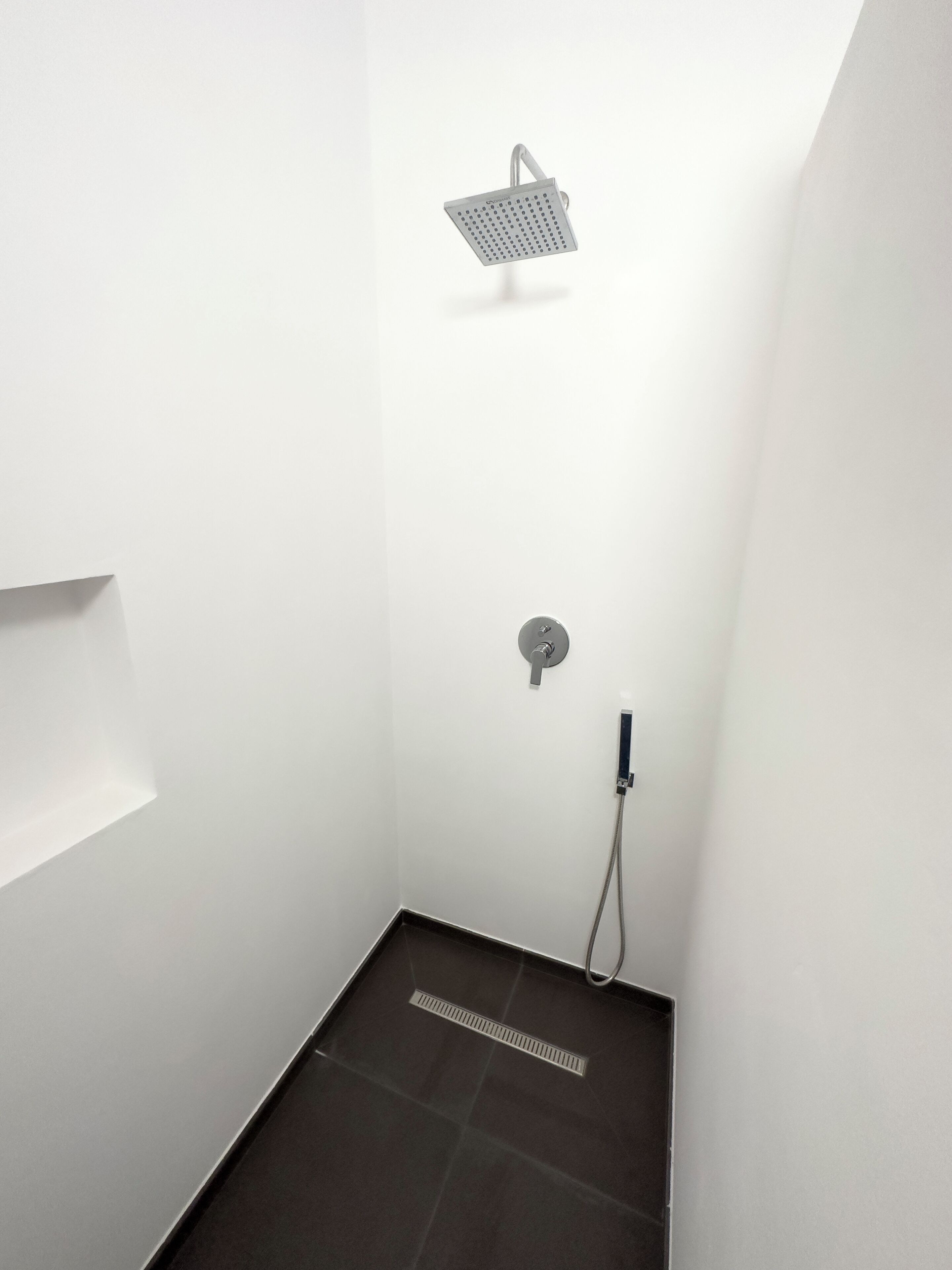 Um banheiro de chuveiro pequeno e moderno, com chuveiro de formato quadrado e torneira fixada na parede.