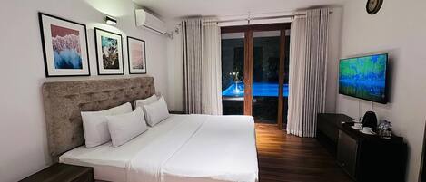 Habitación de hotel con una cama grande, televisión, escritorio y vistas a una piscina exterior.