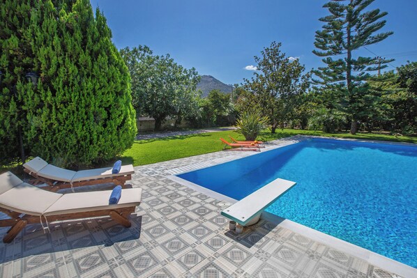 A swimming pool with lounge chairs, a patterned patio, and a mountainous backdrop. - Private villa w/ large pool, walking distance from beach, near Athens (Ag. Panteleimon)