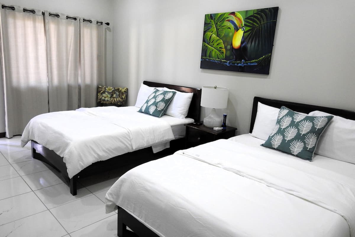 Quarto de hotel com duas camas, roupa de cama branca, mesa de cabeceira com abajur e um quadro na parede.