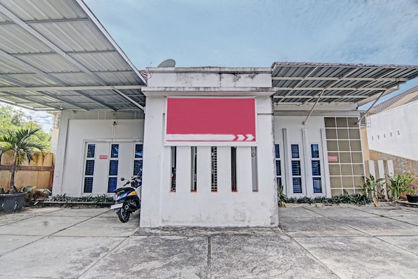 A building with a red banner, a covered parking area, and a motorcycle parked in front. - Hotel O Penginapan Puti SyariahNearBandara Sultan Syarif Kasim II (Pekanbaru)