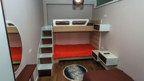 Une petite pièce comprenant un lit superposé, un petit bureau, une chaise et un tapis rond.