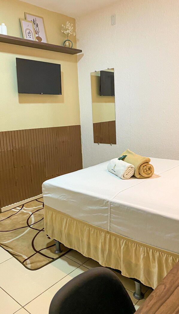 A hotel room with a bed, a mirror, a flat-screen TV, and a small shelf with decorative items. - Pousada Leda Rafael (Joao Camara)