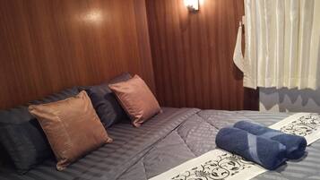 Habitación de hotel con cabecera de madera, cama con ropa de cama gris, dos almohadas marrones y una toalla azul.