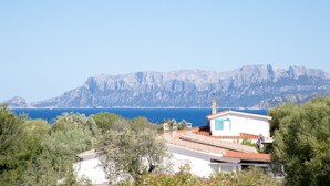Vista costeira com montanha ao fundo, um edifício branco com telhado vermelho e vegetação exuberante em primeiro plano.
