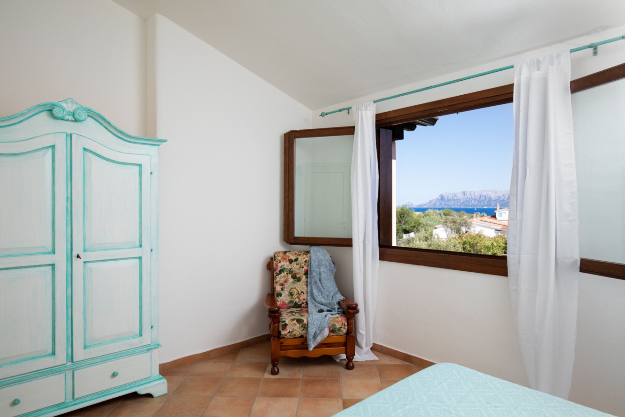 Una habitación con cama, una silla, armario y ventana con vista al paisaje.