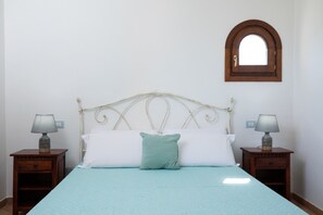 A bed with a white headboard, two bedside tables with lamps, a green pillow, and a small mirror on the wall.