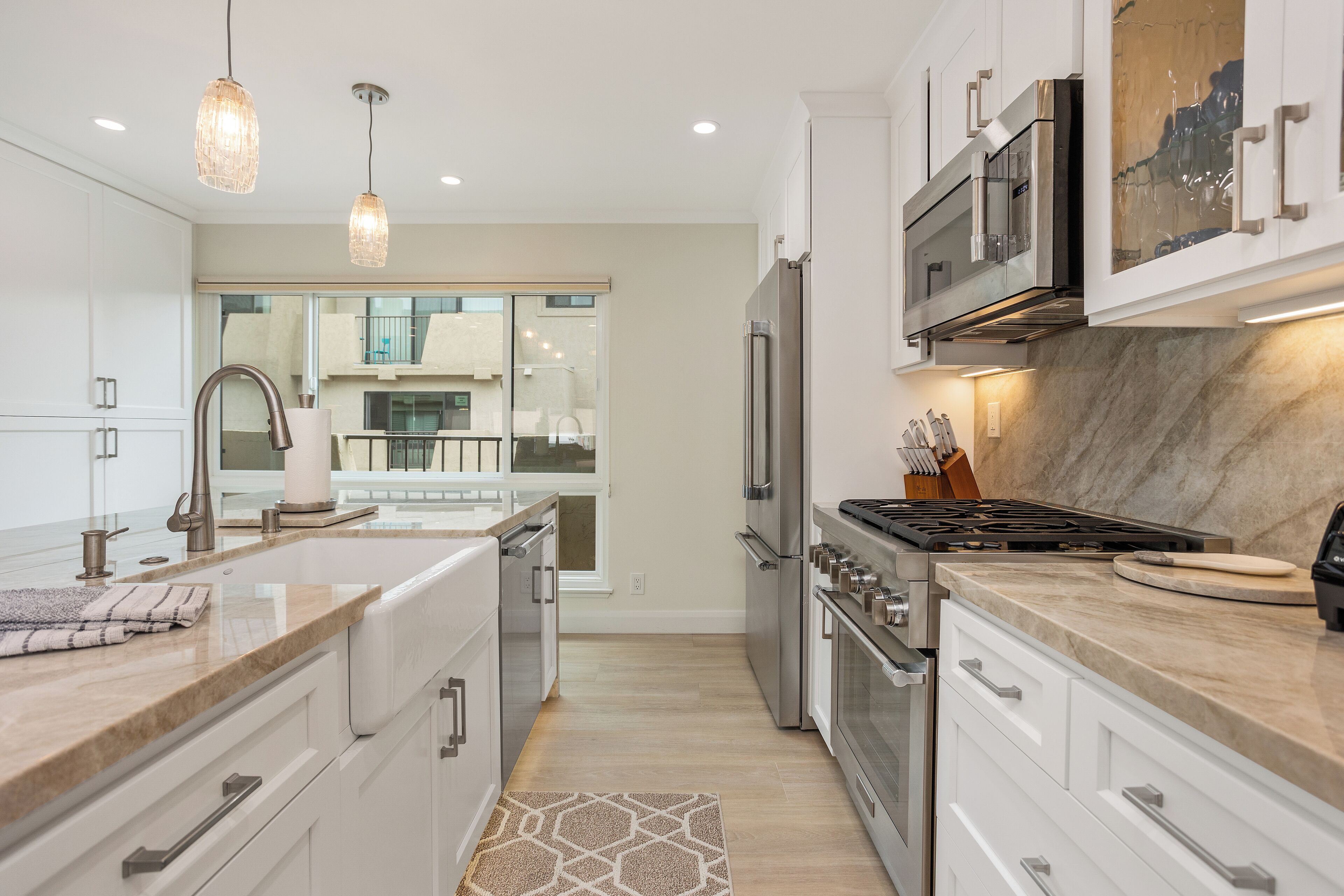 A modern kitchen with white cabinets, stainless steel appliances, and pendant lighting.
