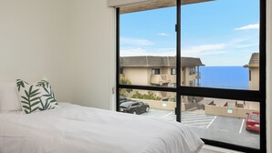 A hotel room with a large window, a bed with white bedding, and a green leaf-patterned pillow. - Pacific Bliss - Ocean View Solana Beach Townhome with Resort Amenities (Solana Beach)