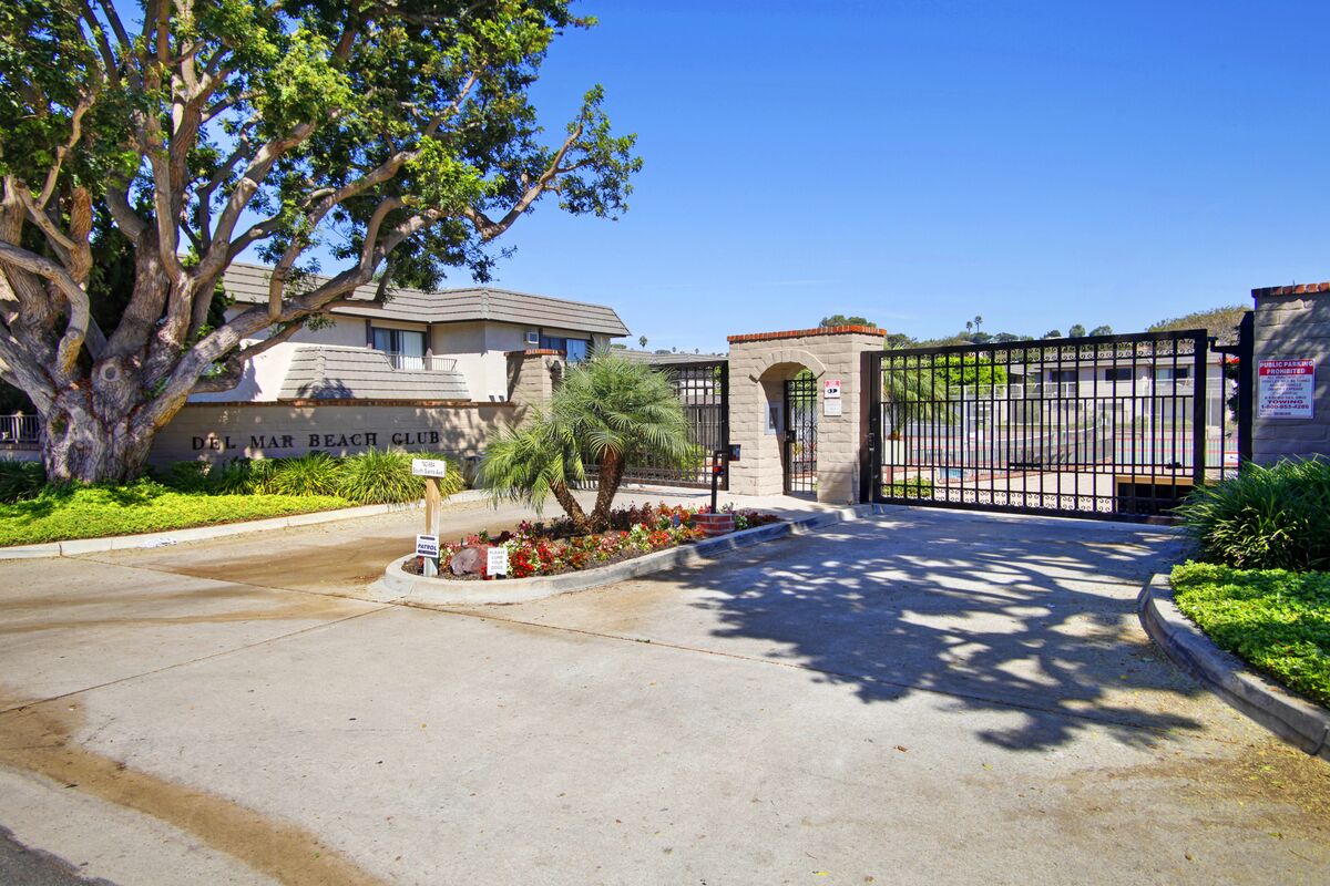A gated entrance to Del Mar Beach Club with a large tree and a signboard.