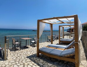 A wooden outdoor seating area with a view of the sea, including a wooden bed and chairs. - Amaltheia Beach Front Houses (Zakynthos)