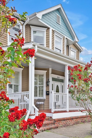 A two-story house with a porch, a number '501' on the front door, and red flowering plants in the foreground.