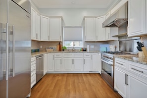 A modern kitchen with white cabinets, stainless steel appliances, and a wooden floor.