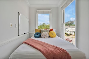 A bedroom with a large window, a bed with a pink blanket, and colorful pillows.