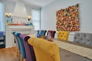 A dining area with a long table, colorful chairs, and a decorative wall with flowers.