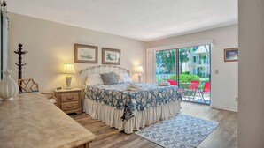 Une chambre à coucher comprenant un lit, des tables de chevet, une commode, une lampe, une fenêtre et une vue sur l’extérieur.