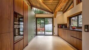 A modern kitchen with wooden cabinetry, a sliding glass door leading to an outdoor patio, and a view of the surrounding landscape. - Peaceful Serviced Chalet with Indoor Pool (Chamonix-Mont-Blanc)