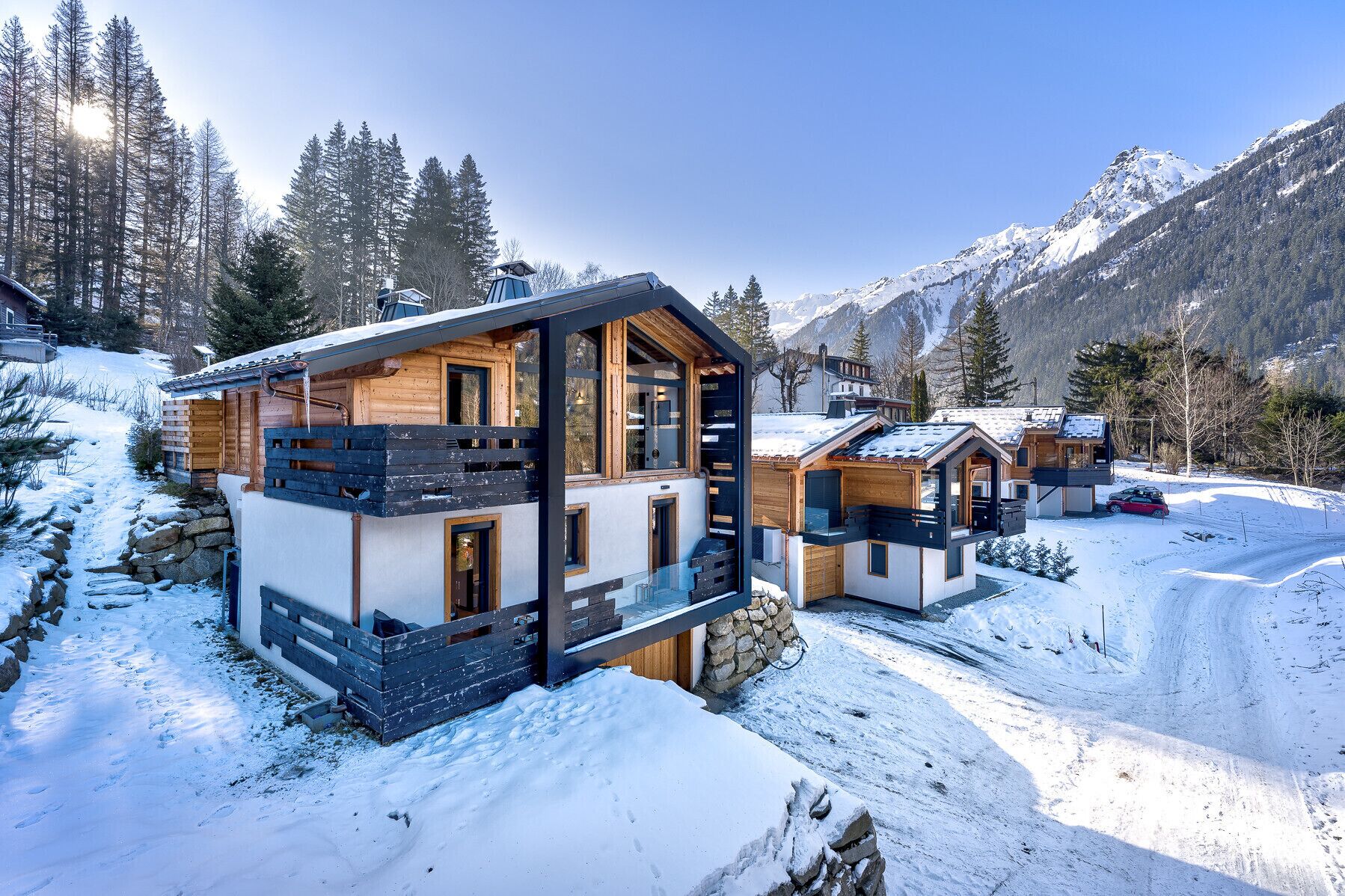Un chalet moderne, doté d’une façade en bois et de grandes fenêtres, entouré de montagnes enneigées et surplombant un ciel dégagé.