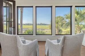 A room with three large windows offering a view of a green landscape and palm trees.