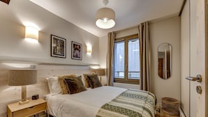 Une chambre à coucher comprenant un lit, une lampe de chevet, des lampes fixées au mur, une fenêtre avec des rideaux, un miroir et un plancher en bois.