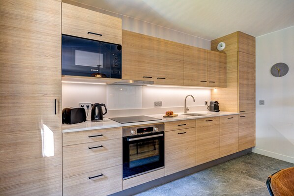 Une cuisine moderne avec des meubles en bois, un four à micro-ondes encastré, une cuisinière et un  évier.