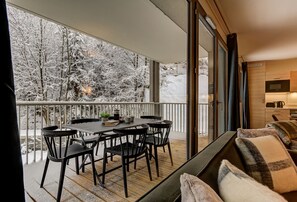 Un balcon avec une table et des chaises, un canapé et un coin cuisine visible à travers une porte vitrée.