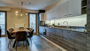 Una cocina moderna con una isla central, armarios de madera oscura y un comedor con mesa y sillas de madera.