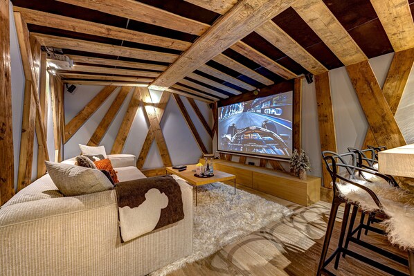 Una habitación acogedora con techo de madera, una pantalla grande, un sofá y una zona de bar.