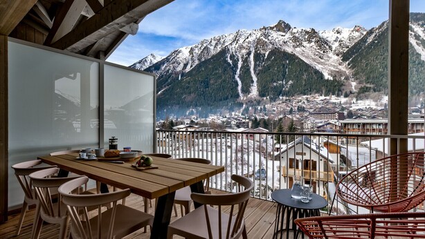A wooden deck with a table and chairs, overlooking a snowy mountain landscape.