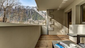 Un balcon avec un plancher en bois, une table avec un magazine et des chaussures, et une vue sur les montagnes.