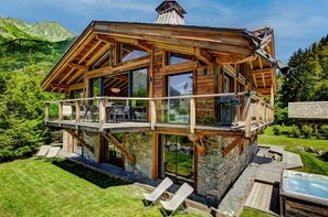 Una cabaña de madera con balcón, cimientos de piedra y un jacuzzi.